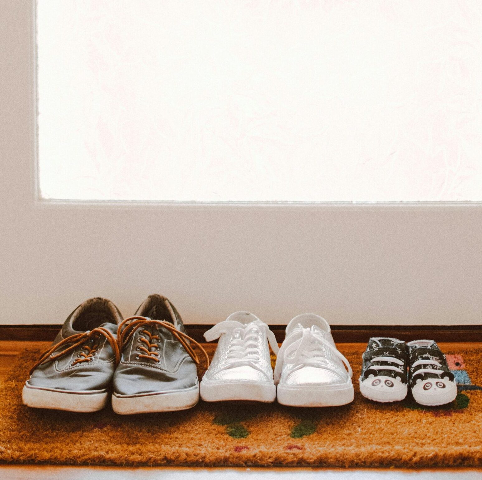 A collection of family shoes, including baby booties, on a welcoming mat by the door.